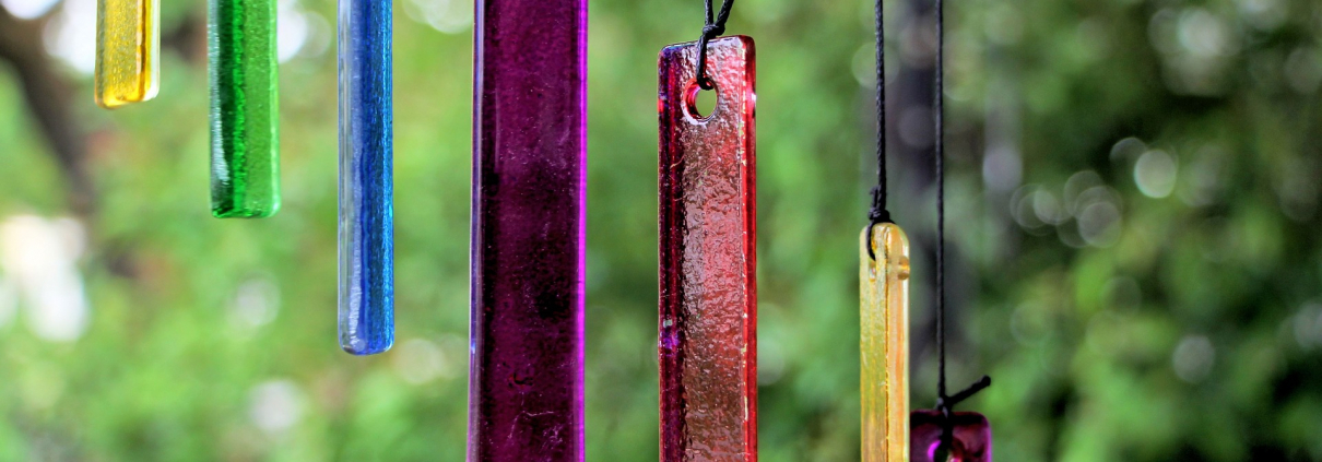 Ein Windspiel aus verschieden farbigen Plättchen hängt in einem Garten.